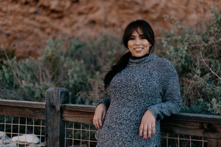 woman-in-a-sweater-smiles-as-she-leans-against-a-fence - Odyssey Street